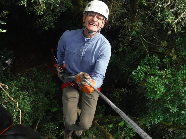 Smiling man in a helmet rappelling or ziplining through a dense forest