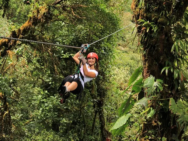 A smiling woman in a red helmet ziplining through a dense tropical forest.