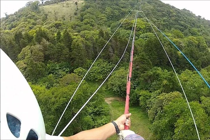 First-person view of ziplining over a vast, dense green forest canopy.