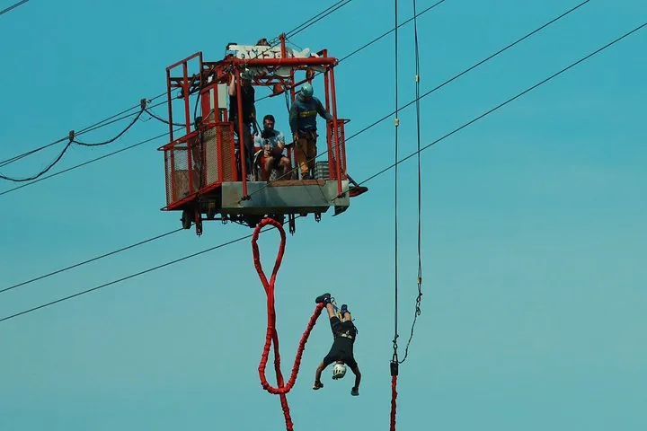 A person bungee jumping upside down from a red aerial tram car.