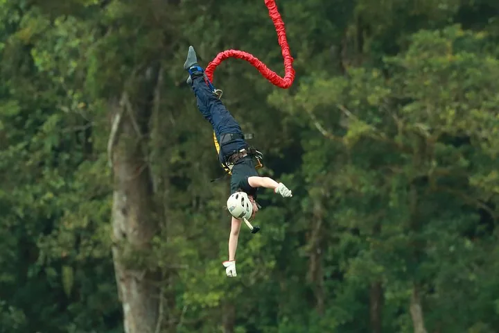 A person bungee jumping with a red cord in a lush green forest.